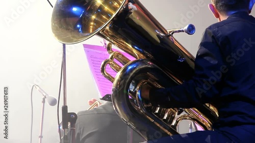 Tubaist in an orchestra on the stage, holds big brass tube, behind the scenes close-up shoot. Musician finished his part and wait photo