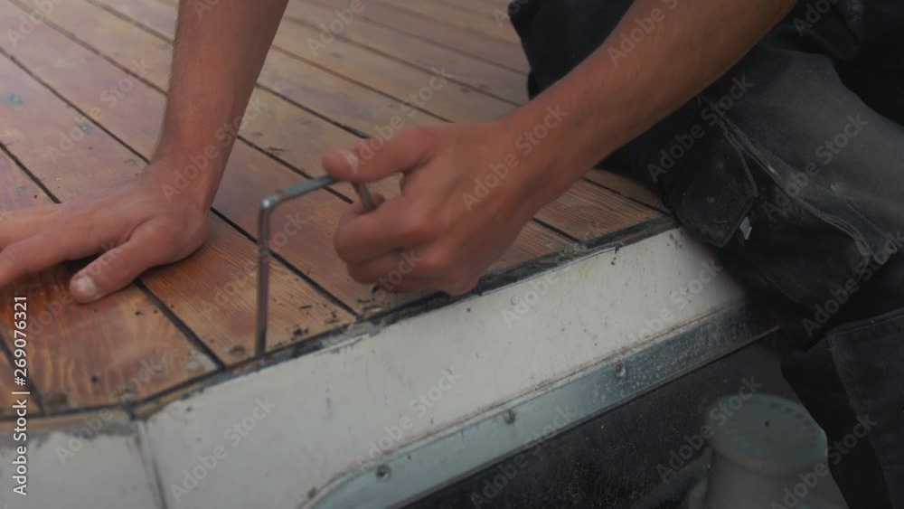 Scraping old mastic sealant between deck planking of wooden boat roof. Scraping old mastic sealant between deck planking of wooden boat roof.