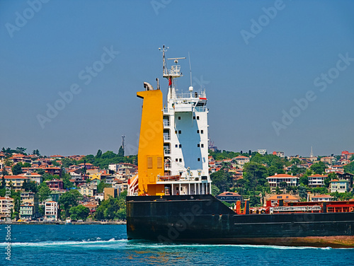 Big cargo ship at Bosporus strait and residential buildings at coast.