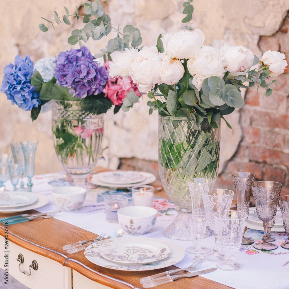 The decor and table setting for a meal or a holiday. Tablewares on a table against a brick wall. A bouquet of colorful flowers. Tableware and decor