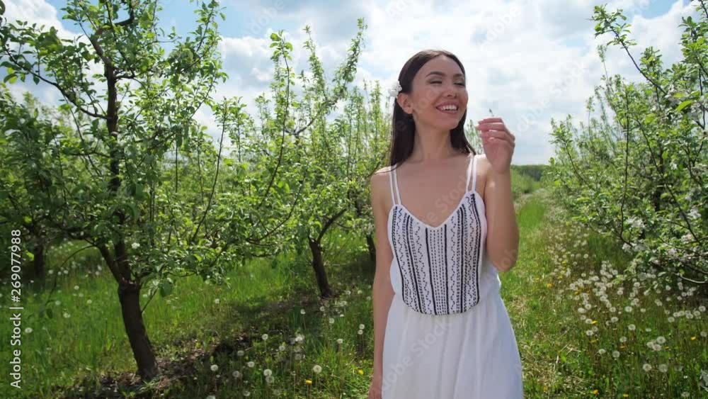 Close-up of beautiful smiling mixed race female enjoying walk among flowering apple trees on sunny spring day. Cheerful asian woman strolling in blooming fruit garden alone Close-up of beautiful smiling mixed race female enjoying walk among flowering apple trees on sunny spring day. Cheerful asian woman strolling in blooming fruit garden alone