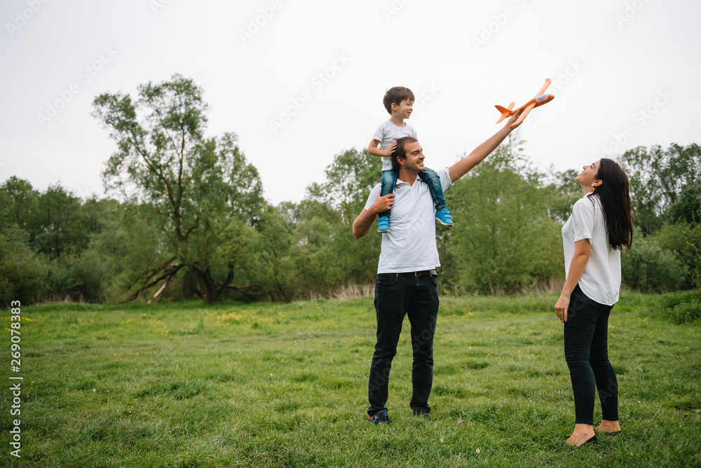 Father, mother and son playing with toy airplane in the park. friendly family. People having fun outdoors. Picture made on the background of the park and blue sky. concept of a happy family. Father, mother and son playing with toy airplane in the park. friendly family. People having fun outdoors. Picture made on the background of the park and blue sky. concept of a happy family.