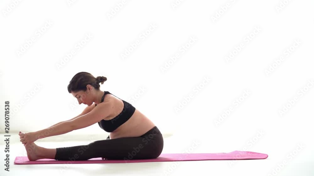 Pregnant brunette girl doing yoga on a white background. Authentic style with natural light and shadows. Pregnant brunette girl doing yoga on a white background. Authentic style with natural light and shadows.