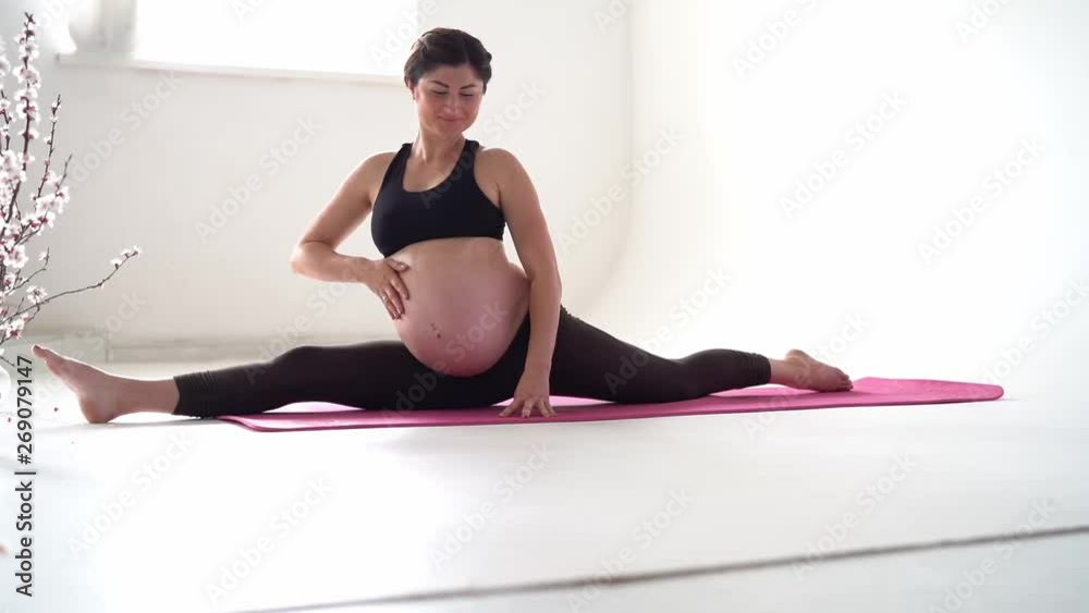 Pregnant brunette girl doing yoga on a white background. Authentic style with natural light and shadows.