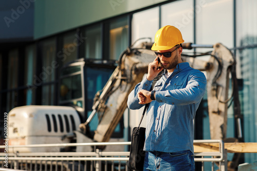 Construction engineer talking on the phone and looking at the watch on the construction site photo