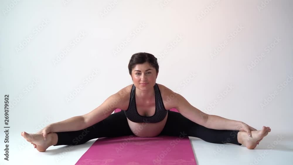 Pregnant brunette girl doing yoga on a white background. Authentic style with natural light and shadows. Pregnant brunette girl doing yoga on a white background. Authentic style with natural light and shadows.