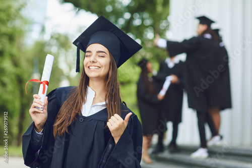 A young female graduate with a scroll background of university graduates.