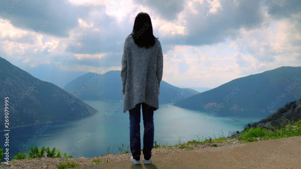 back view woman standing in mountain area female wearing casual sweater and sneakers amazing landscape cloudy sky replaced by sun weather changes