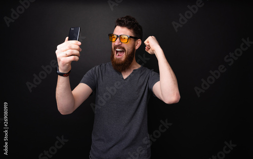 Obraz na płótnie Photo of excited bearded man holding mobile, scraming and celebraing with rised