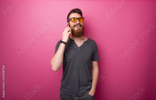 Portrait of handsome  bearded man talking on phone with firends over isolated pink background