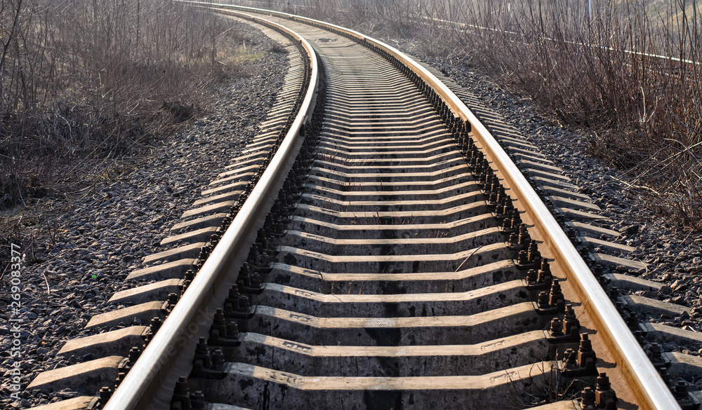 Obraz premium Wide railroad track with concrete sleepers (cross ties), turning left, close-up, backlight, selective focus
