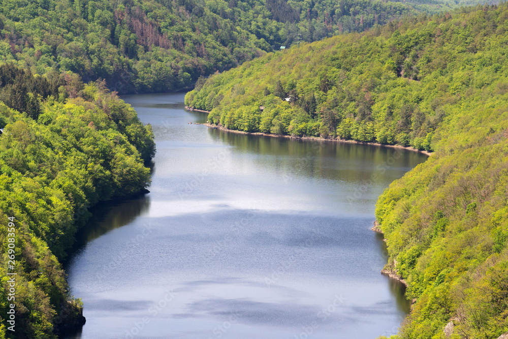 Fototapeta premium Solitary beautiful cottage in breathtaking green woods over banks of river, calm water surface, nature landscape, sunny summer day, secluded dwelling, hermitage, Vltava, Slapy reservoir dam