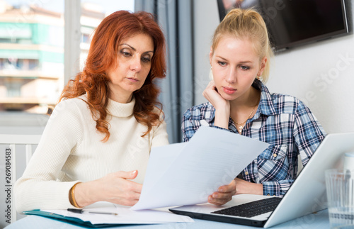 Sad mature woman and daughter signing documents at table with laptop