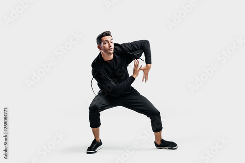 Dark-haired young man dressed in a black clothes is dancing street dance. He makes stylized movements with his hands