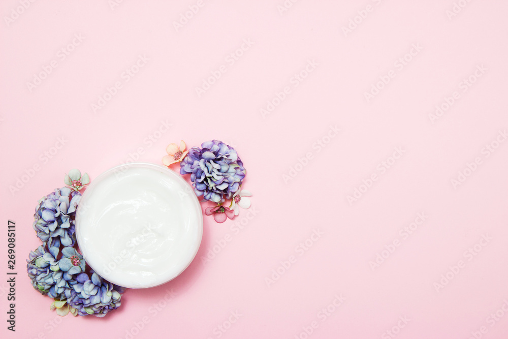 A jar of cream with flowers on a pink background. Top view. A jar of cream with flowers on a pink background. Top view.