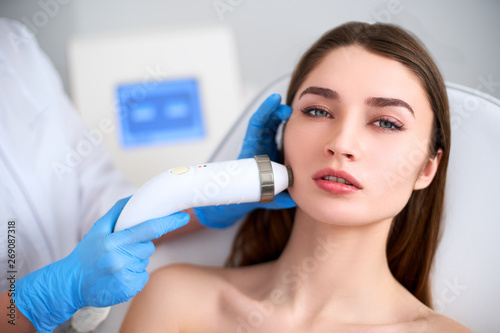 Photography Beautician doctor doing rf-lifting procedure for flawless woman face laying in a beauty salon