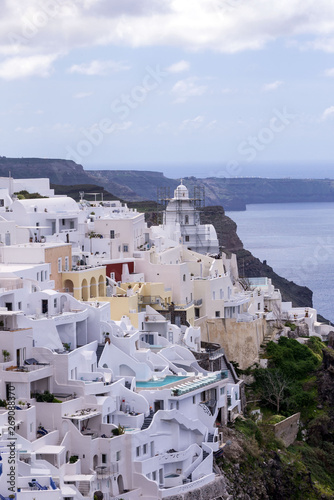 White traditional Greek houses on a hillside on the island of Santorini. Beautiful view of the sea, the ship, the volcano and buildings on a sunny day. Reconstruction of the church and restaurants.