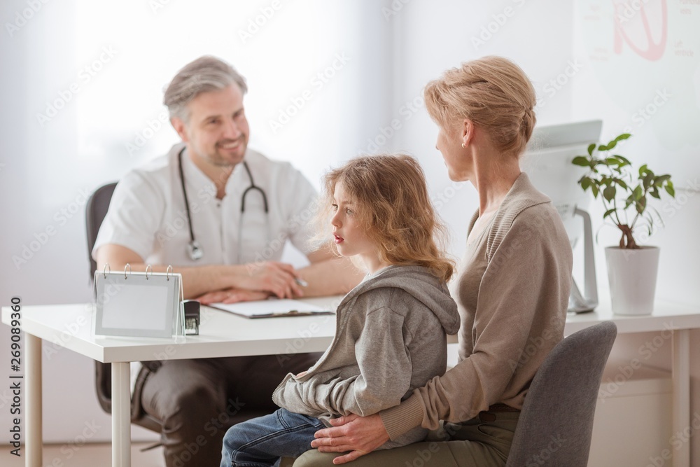 Mom and cute sick son in front of the handsome pediatrician's desk