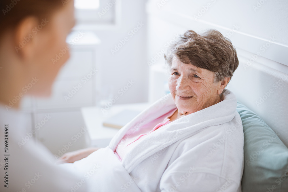 Fototapeta premium Elderly woman in white bathrobe and young volunteer at nursing home