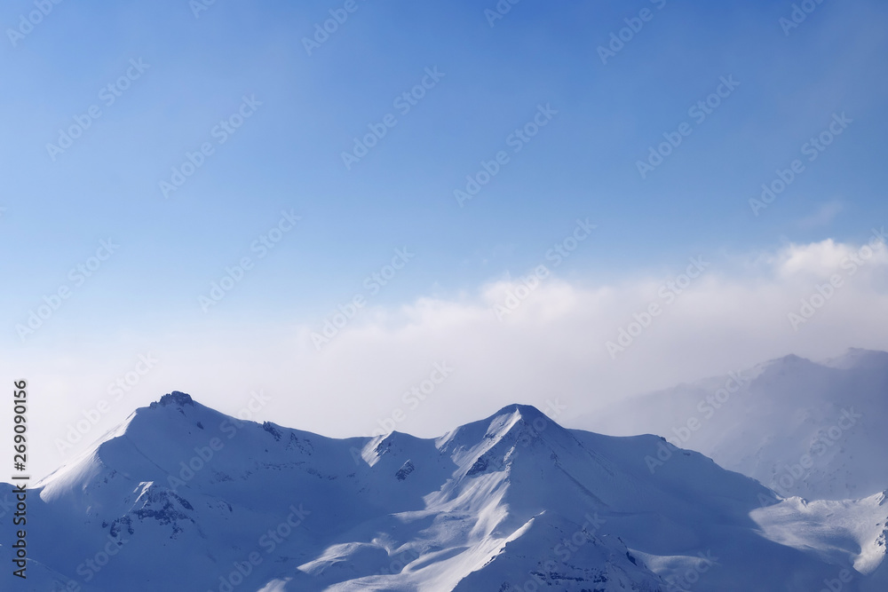 High snowy mountains in mist and sunlit cloudy sky at winter evening