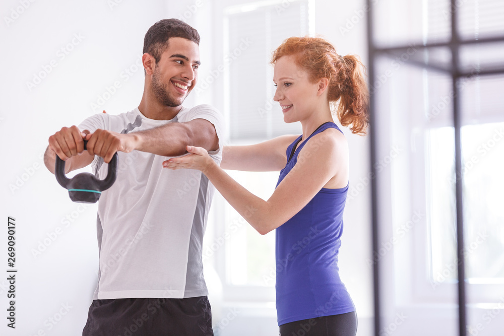 Smiling sportsman with weight during workout with personal trainer Smiling sportsman with weight during workout with personal trainer