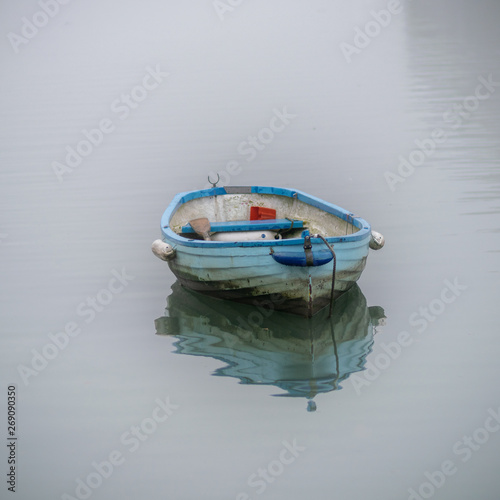 Small boat on clam water with reflection and mist.