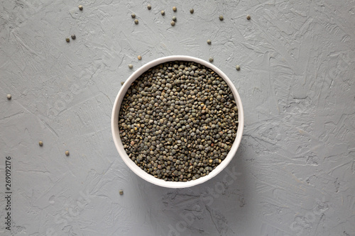 Dry green french lentils in a bowl over gray background, top view. Overhead, from above, flat lay.