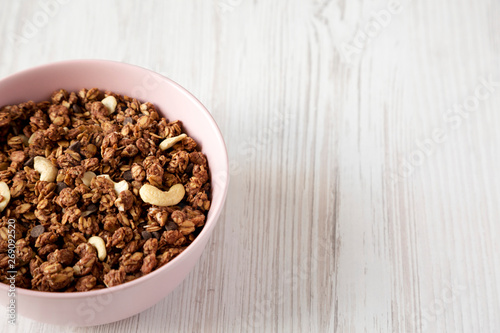 Homemade chocolate granola with nuts in a pink bowl, low angle view. Space for text.