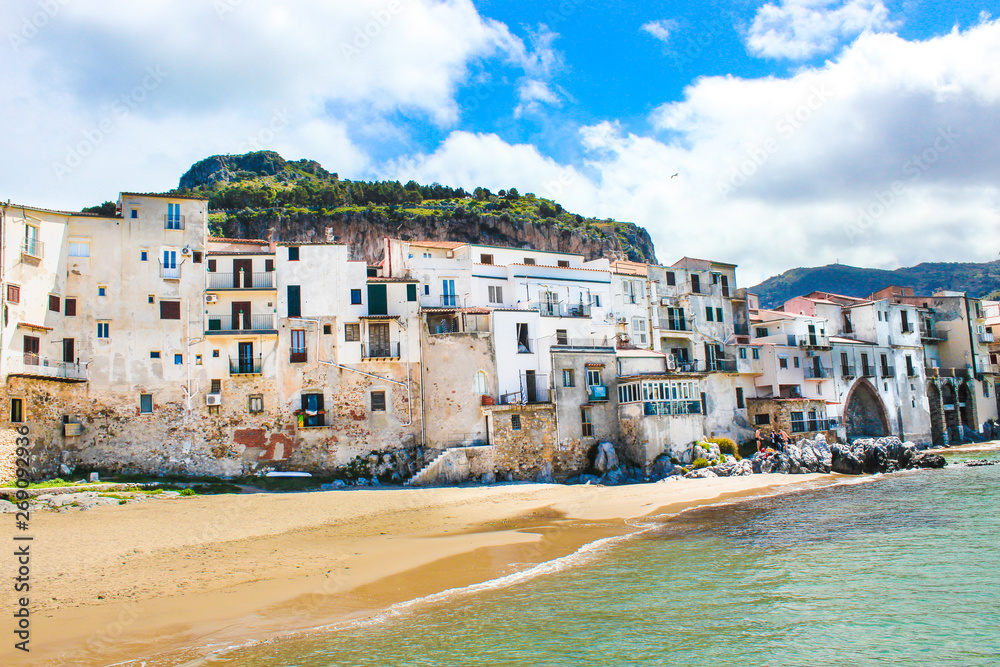 Traditional historical houses on the coast of Tyrrhenian sea in Sicilian Cefalu, Italy. Behind the houses there is rock overlooking the city. The beautiful Italian city is a popular tourist attraction