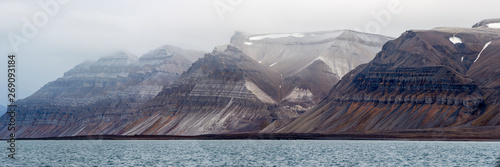 Billon year old jagged rock formations with different green moss and snow within, Svalbard, Isfjorden, Norway photo