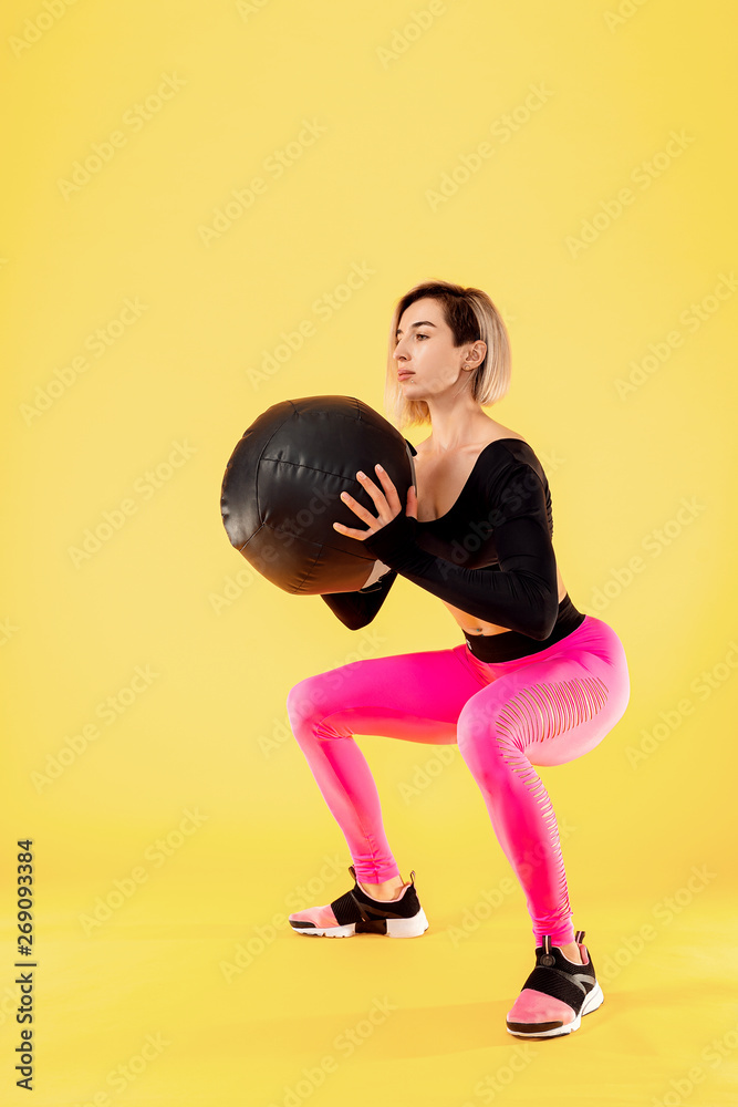 Strong woman workout with med ball. Photo of sporty latin woman in fashionable sportswear on yellow background. Strength and motivation.