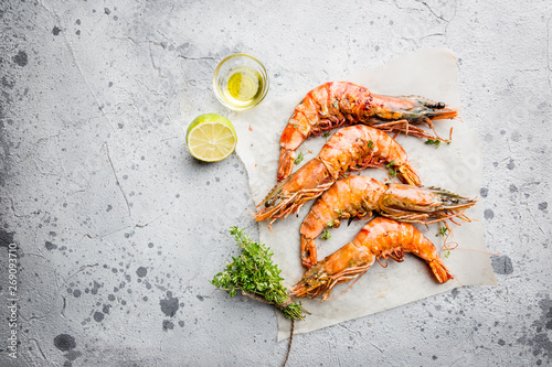 Grilled giant tiger prawns on paper with lemon and spices on light gray background, top view, copy space. Seafood dinner. photo