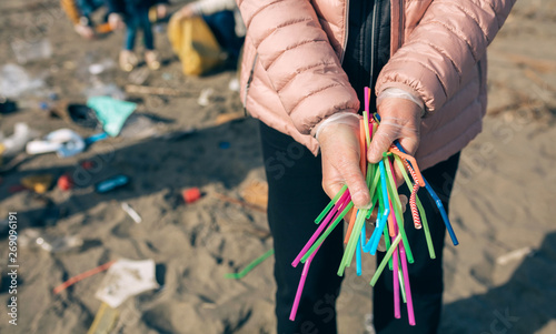 Fotografie Unrecognizable woman showing handful of straws collected on the beach with group of volunteers working in the background
