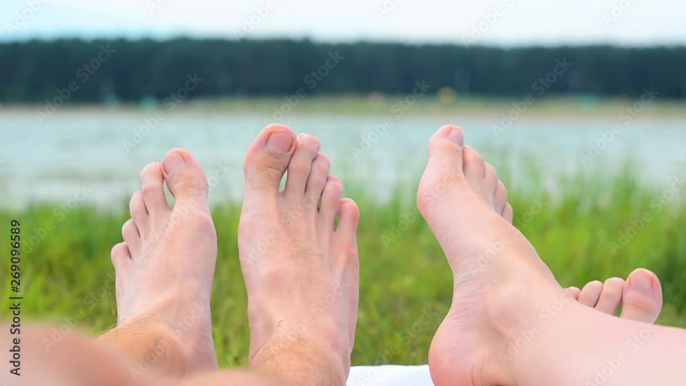 Close up of young couple feet relaxing on beach. Woman. Man. Lake. Landscape. Legs. Blur Background Close up of young couple feet relaxing on beach. Woman. Man. Lake. Landscape. Legs. Blur Background