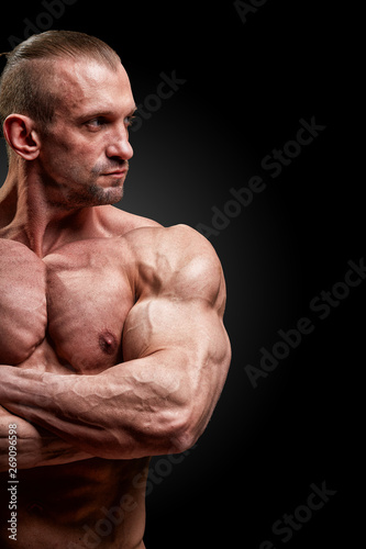 Sport concept. Fitness athlete with perfect muscles poses on camera over black background.