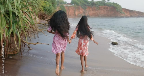 Two Young South Asian sisters with lush and beautiful hair run down the beach holding hands. Girls are laughing and look very happy. tracking shot. in slow motion. Shot on Canon 1DX mark2 4K camera photo