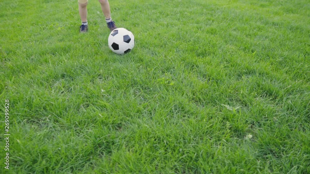 Boy playing soccer ball. Child with the ball runs through the green grass. Children's sport. Family holiday. The boy dreams of becoming a famous footballer. Training. Health. Happy childhood. Boy playing soccer ball. Child with the ball runs through the green grass. Children's sport. Family holiday. The boy dreams of becoming a famous footballer. Training. Health. Happy childhood.