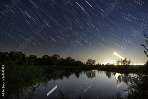 Trail of stars in the night sky around the North Star over the lake. photographed with a long exposure on the background. © olgapkurguzova