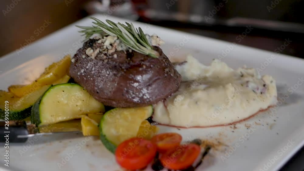 camera turns around filet mignon dish. A server sets down a plated filet mignon steak with steamed vegetables and mashed potatoes on a restaurant table. camera turns around filet mignon dish. A server sets down a plated filet mignon steak with steamed vegetables and mashed potatoes on a restaurant table.