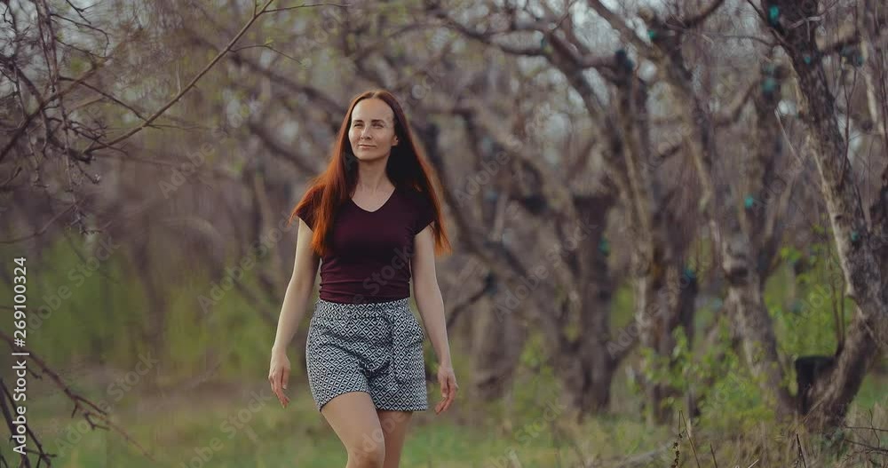Happy pretty woman walks among the trees and enjoys nature. Early spring leaves are growing on the trees. Happy pretty woman walks among the trees and enjoys nature. Early spring leaves are growing on the trees.