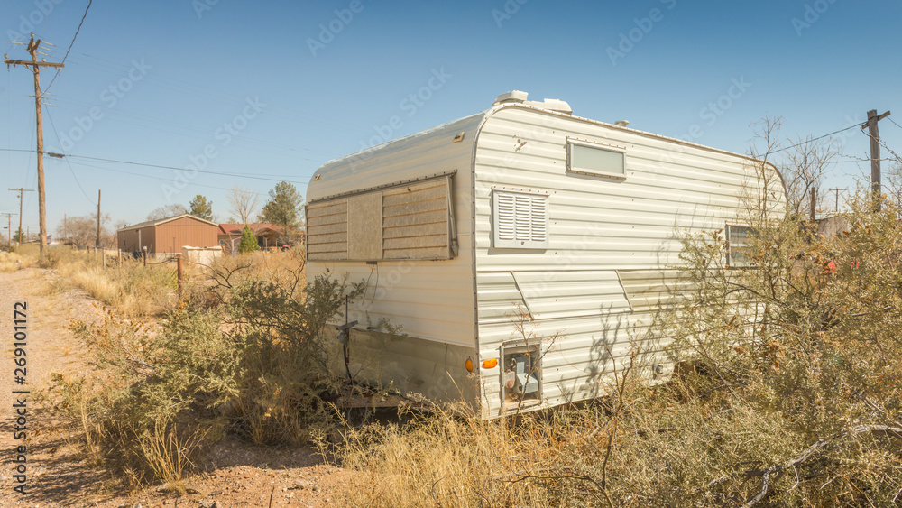 Retro abandoned travel trailer RV in an overgrown yard