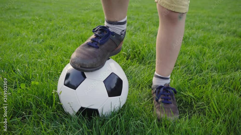 boy puts his foot on a soccer ball. brown shoes. worn sneakers, boots. ball on green grass. children's sport. family holiday. the boy dreams of becoming a famous footballer. training. health. happy boy puts his foot on a soccer ball. brown shoes. worn sneakers, boots. ball on green grass. children's sport. family holiday. the boy dreams of becoming a famous footballer. training. health. happy