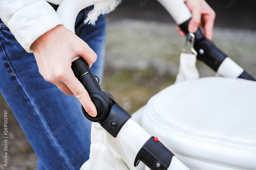 Woman strolling with baby-carriage. Close up of female hands change adjustable handle baby-carriage.
