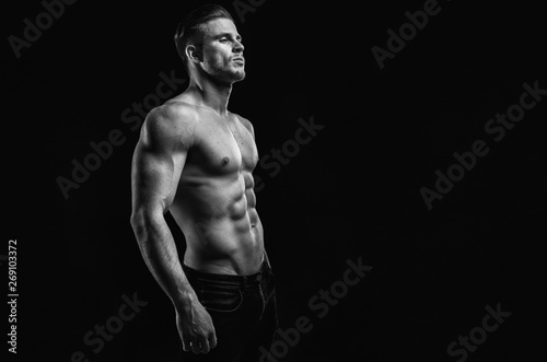 Muscular model young man on dark background. Black and white fashion portrait of strong brutal guy with modern trendy hairstyle. Sexy naked torso six pack abs. Male flexing his muscles. Sport concept.