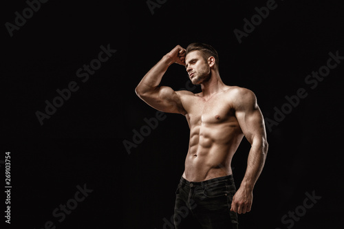 Muscular model young man on dark background. Fashion portrait of strong brutal guy with trendy hairstyle. Sexy naked torso, six pack abs. Male flexing his muscles. Sport workout bodybuilding concept.