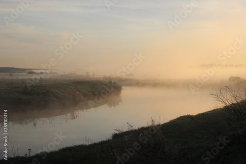 Mist above calm river water in early summer morning
