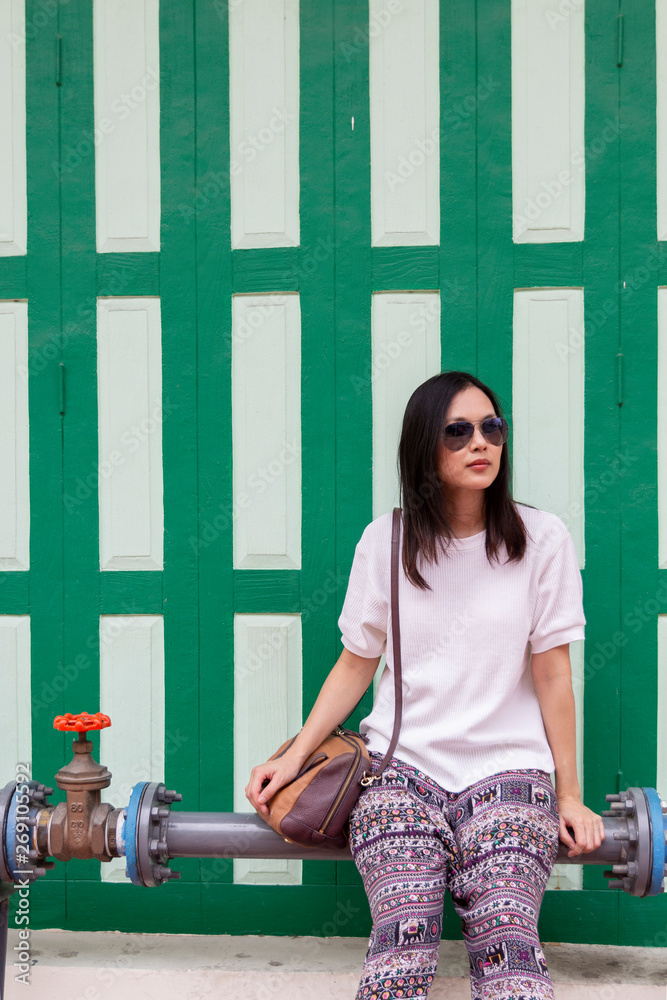 Beautiful pretty young Asian teenage lady girl with sunglasses sitting on big water pipe and waiting friend, taxi, bus or tram with brown handbag under bright clear sky with copy space Beautiful pretty young Asian teenage lady girl with sunglasses sitting on big water pipe and waiting friend, taxi, bus or tram with brown handbag under bright clear sky with copy space