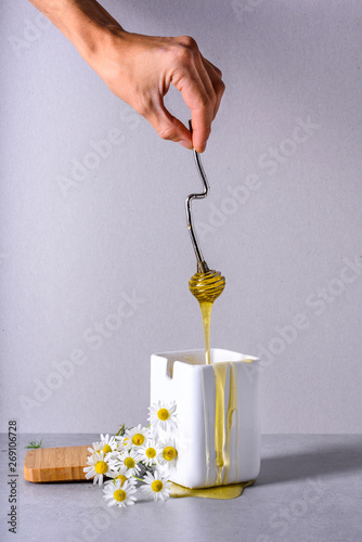 Honey, hand pouring sweet healthy nectar in a white pot