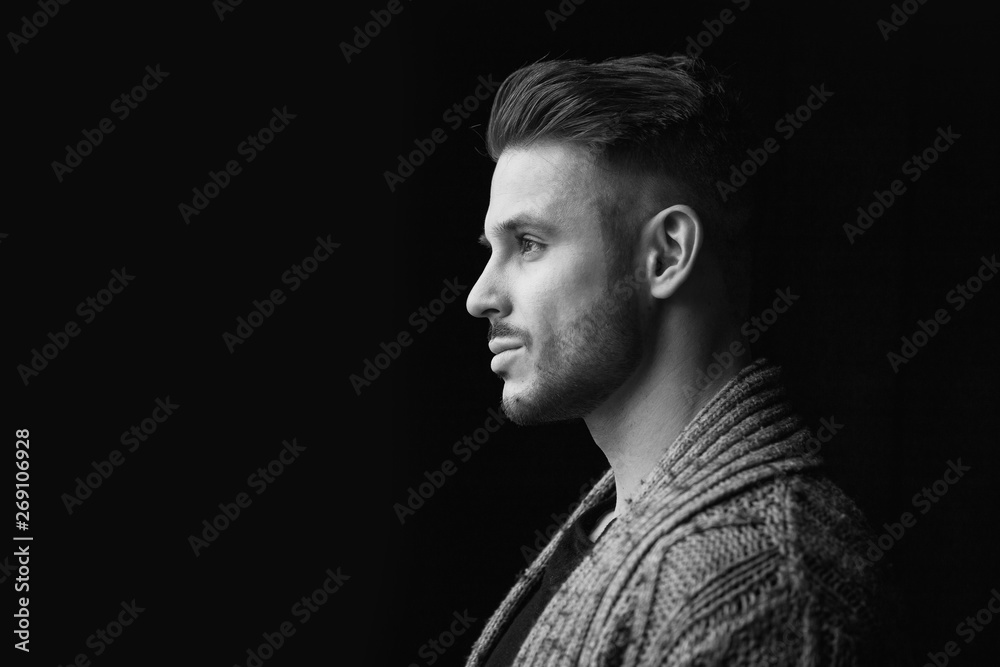 Black and white. Muscular model young man with beard in knitted sweater on dark background. Fashion portrait of brutal sporty sexy strong guy with modern trendy hairstyle. Model, fashion concept.