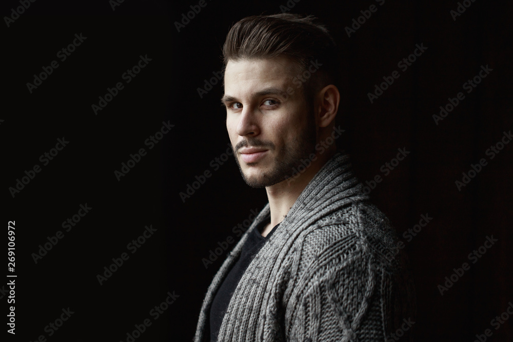 Muscular model young man with beard in knitted sweater on dark background. Fashion portrait of brutal sporty sexy strong muscle guy with modern trendy hairstyle. Model, fashion concept. Muscular model young man with beard in knitted sweater on dark background. Fashion portrait of brutal sporty sexy strong muscle guy with modern trendy hairstyle. Model, fashion concept.